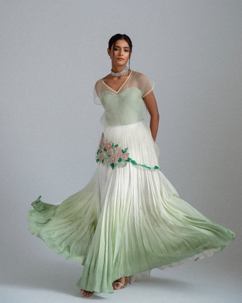 Organza top with delicate floral motifs, accompanied by a sage green bustier and an ombré-layered asymmetrical skirt. 