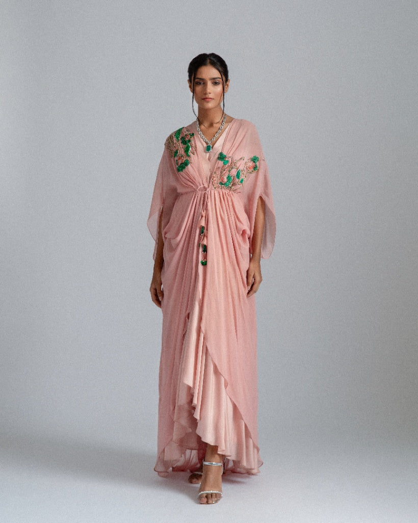 A Peach asymmetrical drape dress paired with a kaftan jacket featuring intricate green and champagne-toned floral embroidery and accentuated by a pleated box opening inner drape. 