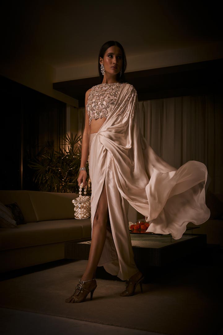 An ivory pre-draped saree in pure silk satin paired with a heavily hand-embroidered blouse featuring intricate pearl and sequin detailing.