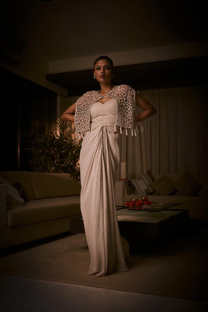 Ivory draped dress paired with a geometric embellished cape jacket, finished with  pearl tassels.