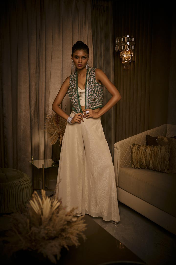 An ivory crushed fabric set featuring flared pants, a crystal-detailed bustier, and an embellished green jacket.