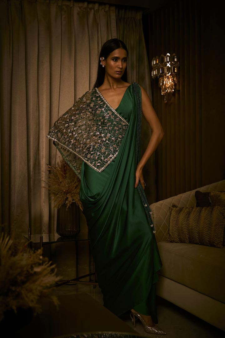 An emerald green pure silk satin draped saree paired with an intricately embroidered tulle cape.