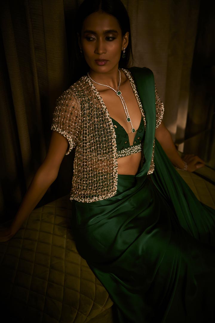 An emerald green pure silk satin pre-draped saree paired with a beaded bralette and embellished cutwork cape.