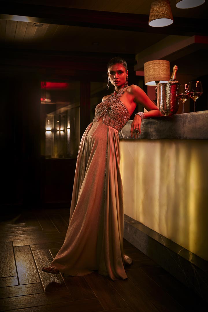 A taupe crushed fabric jumpsuit with a hand-embroidered halter neckline and satin drape detailing.