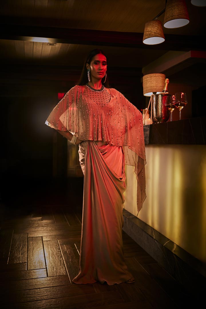 Taupe three-piece ensemble featuring a draped skirt, structured blouse, and a sheer embellished cape.