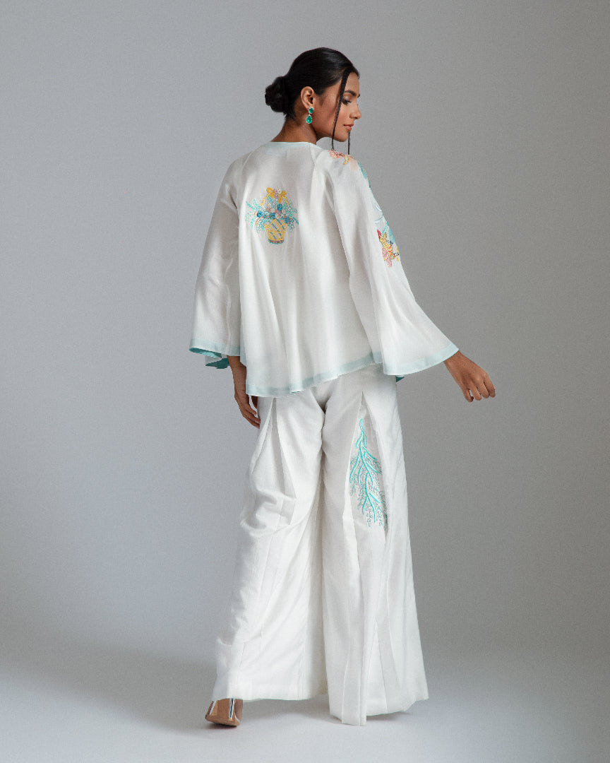 White asymmetrical jacket complemented by chanderi silk pleat flairs and a hand-embroidered net bustier.
