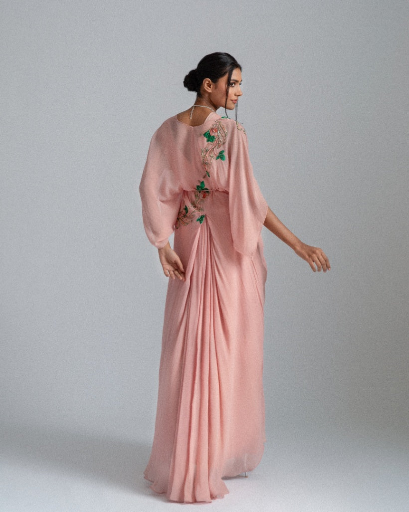 A Peach asymmetrical drape dress paired with a kaftan jacket featuring intricate green and champagne-toned floral embroidery and accentuated by a pleated box opening inner drape. 