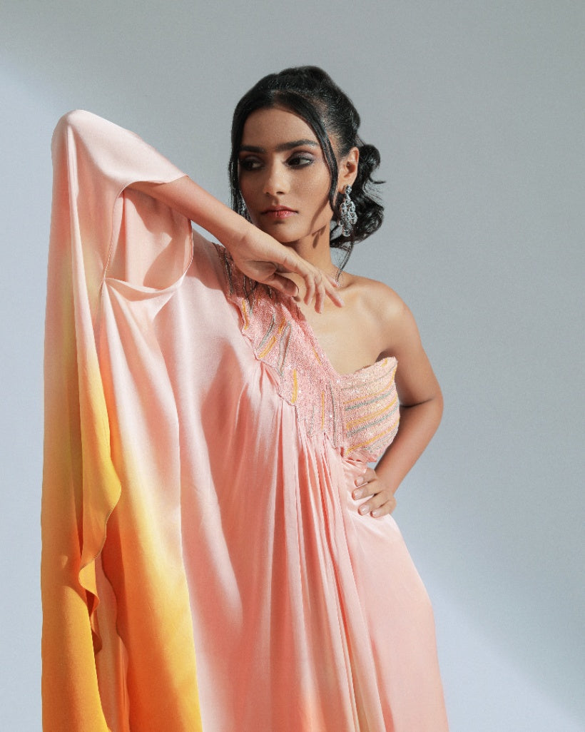 A one shoulder drape dress with a gradient from peach to vibrant orange, adorned with tone-to-tone beadwork. 