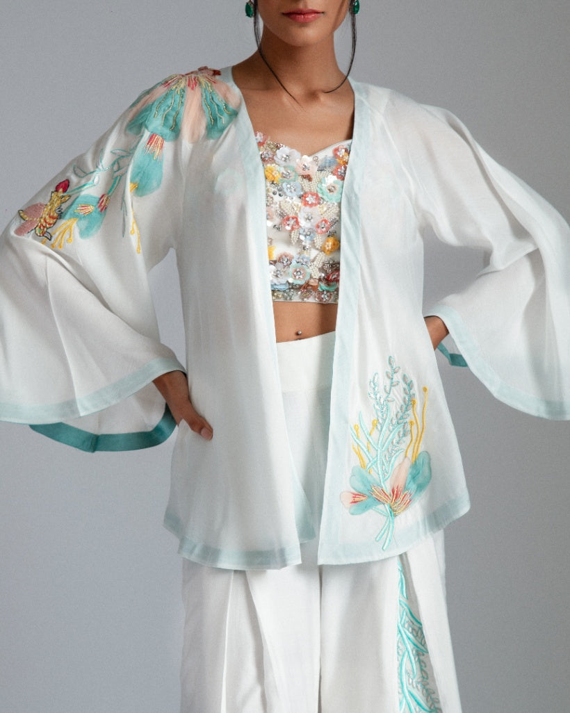 White asymmetrical jacket complemented by chanderi silk pleat flairs and a hand-embroidered net bustier.