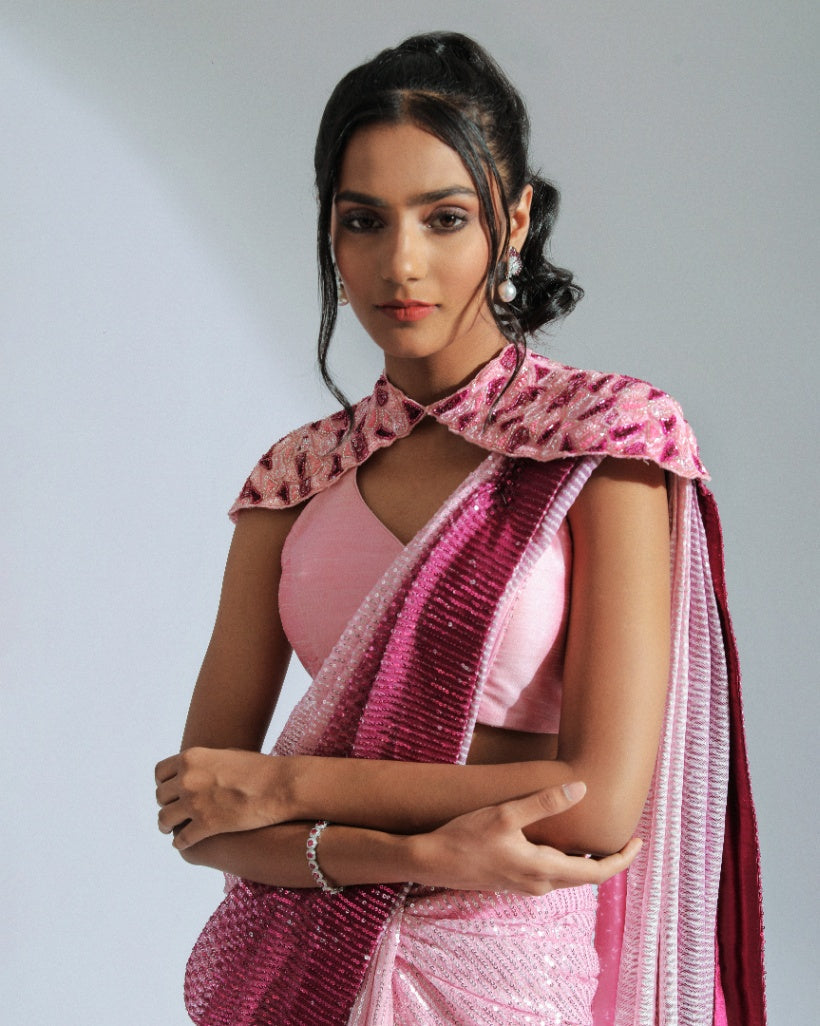 A georgette ombré saree transitioning from light to vibrant shades of Fuchsia pink with sequin lines, accompanied by a cut silk blouse and a removable embroidered shoulder cape. 