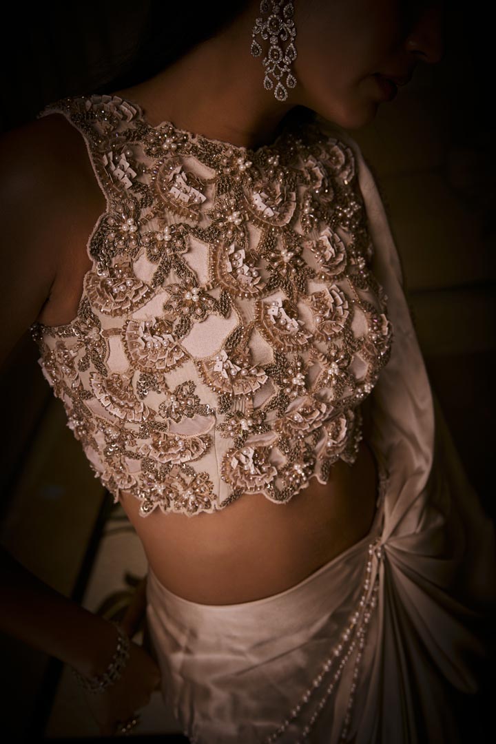 An ivory pre-draped saree in pure silk satin paired with a heavily hand-embroidered blouse featuring intricate pearl and sequin detailing.
