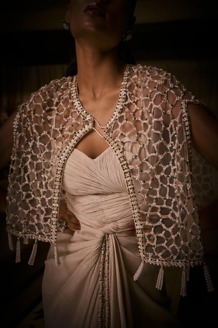 Ivory draped dress paired with a geometric embellished cape jacket, finished with  pearl tassels.