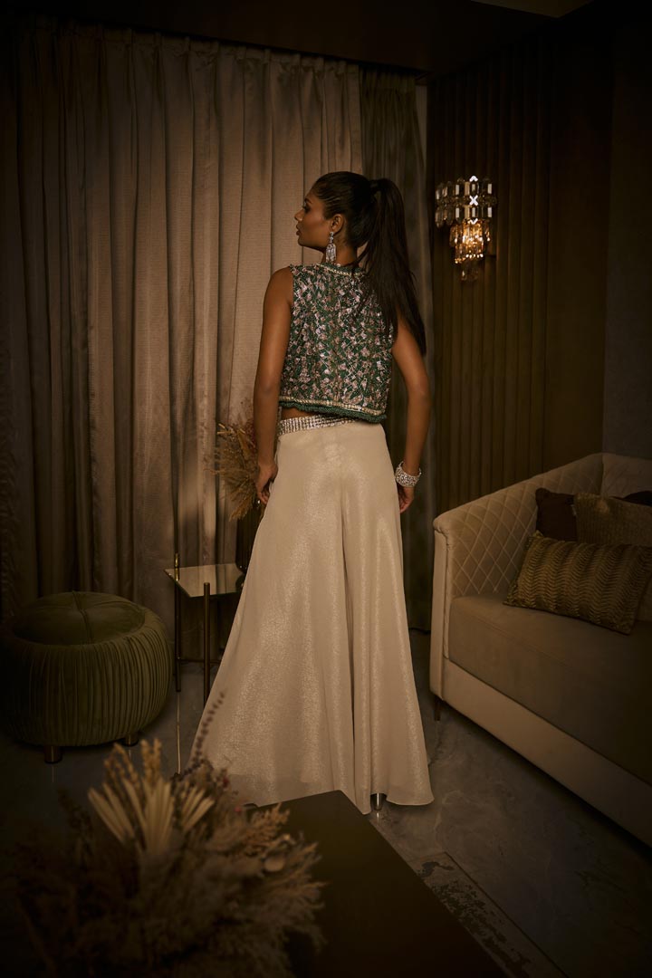 An ivory crushed fabric set featuring flared pants, a crystal-detailed bustier, and an embellished green jacket.