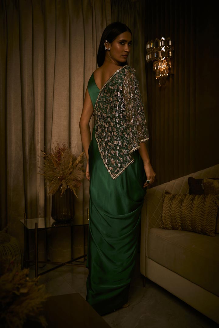 An emerald green pure silk satin draped saree paired with an intricately embroidered tulle cape.