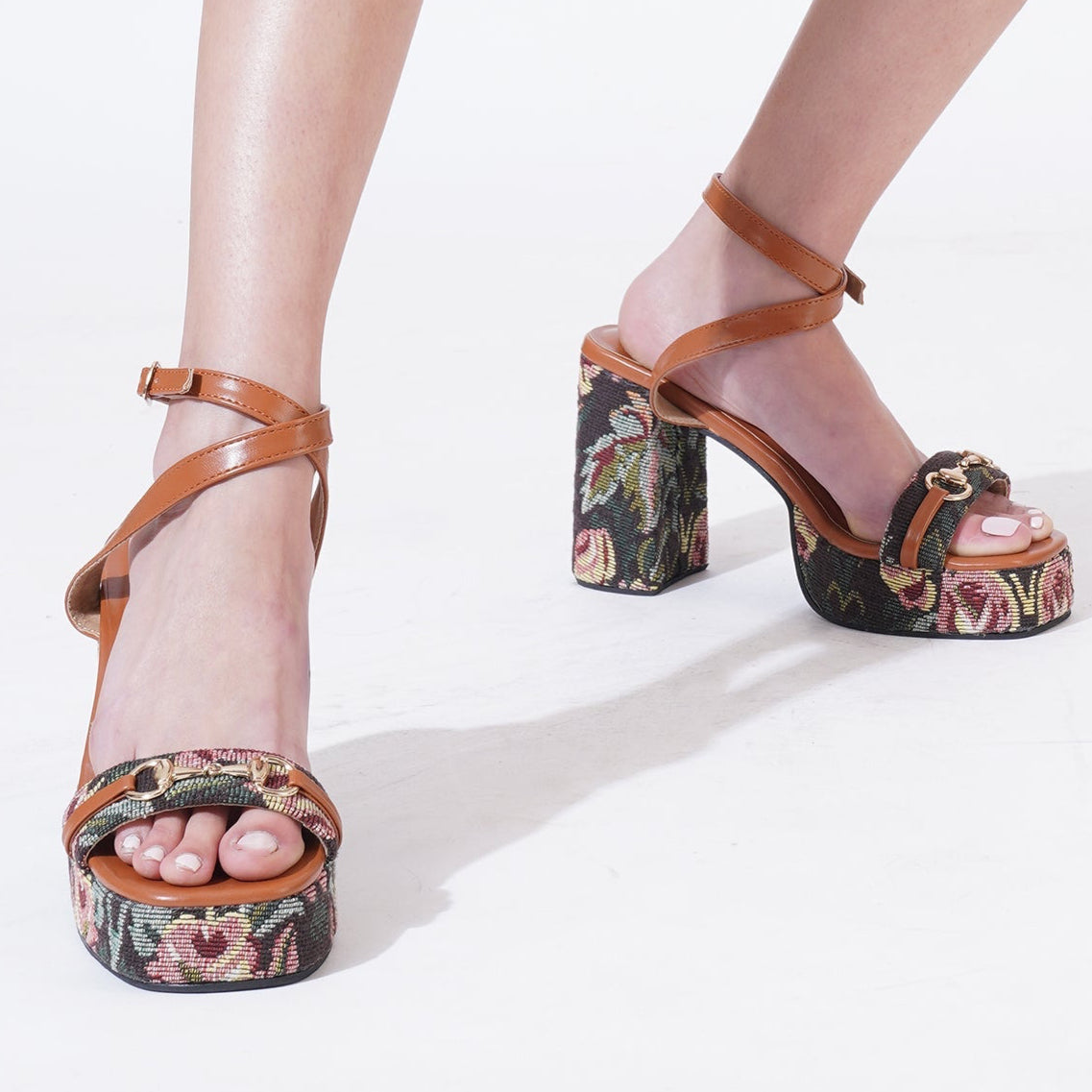 A pair of jacquard, 4-inch block heel sandals with floral tapestry design and tan vegan leather straps, featuring horse bite buckle details.