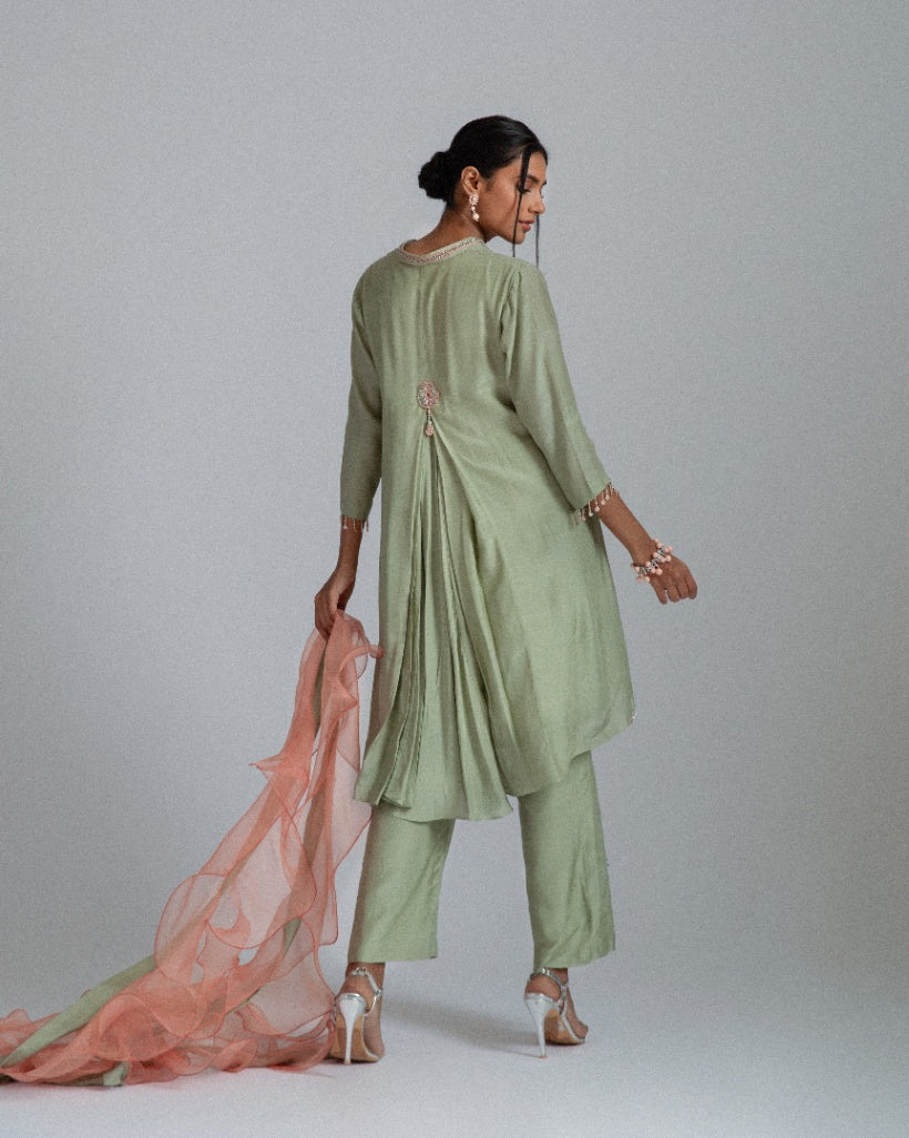 A sage green Silk mul mul tunic shirt with unique back box pleat, embellished with floral motifs, complemented by motif trousers and a peach organza ruffle scarf. 