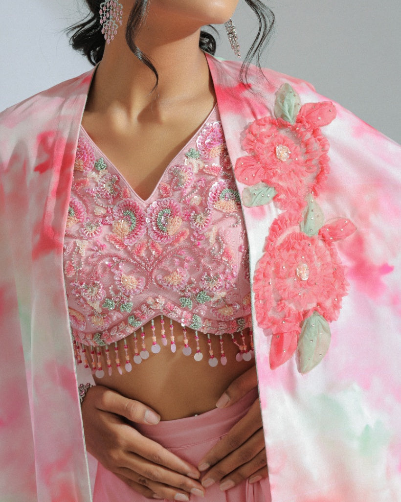 A Georgette cape in pink and sage ombré tones adorned with organza floral patterns and an inner hand-embroidered blouse with a pink modal satin lungi drape. 