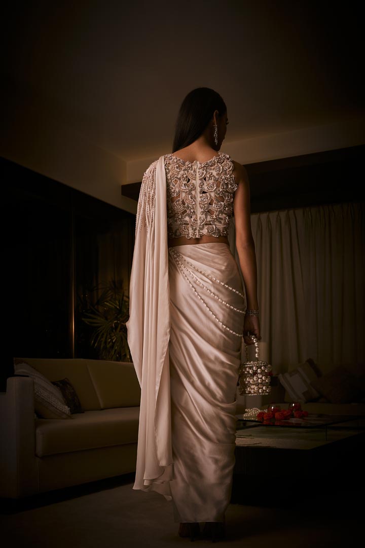 An ivory pre-draped saree in pure silk satin paired with a heavily hand-embroidered blouse featuring intricate pearl and sequin detailing.