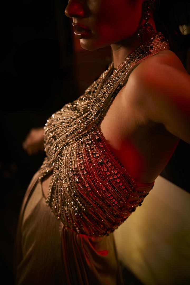 A taupe crushed fabric jumpsuit with a hand-embroidered halter neckline and satin drape detailing.