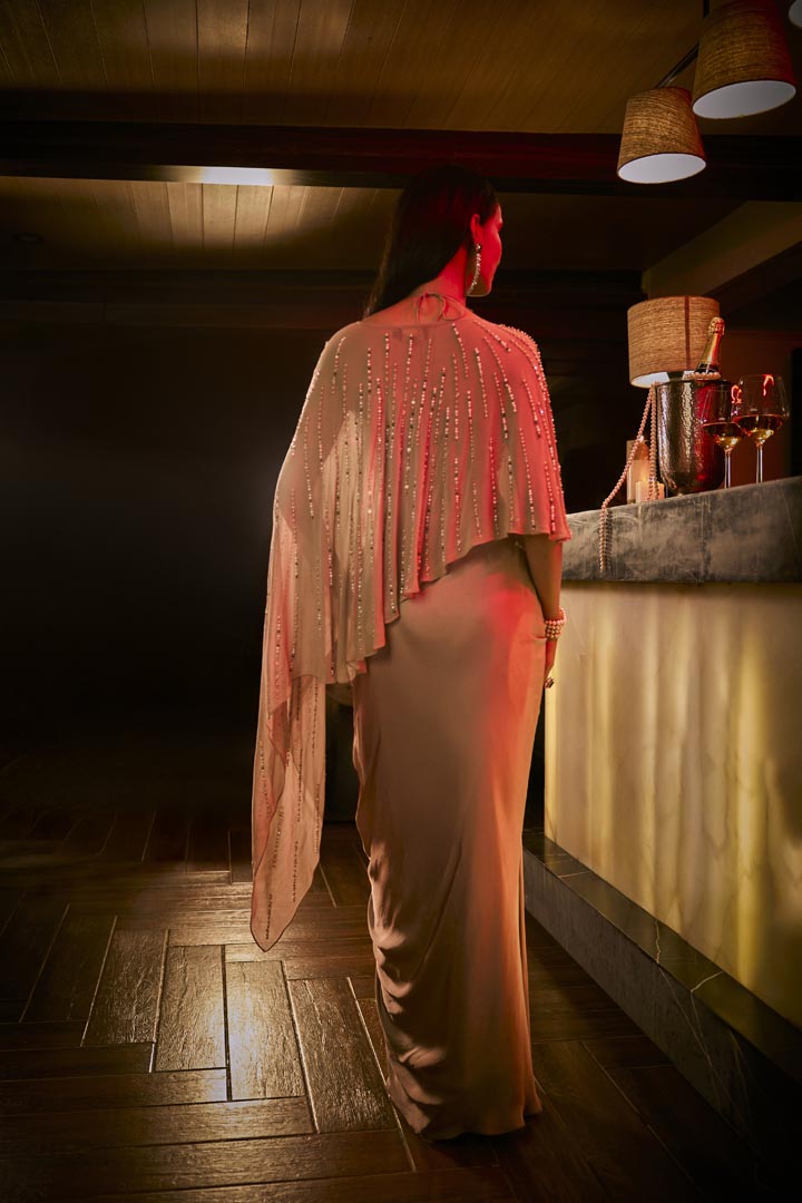 Taupe three-piece ensemble featuring a draped skirt, structured blouse, and a sheer embellished cape.