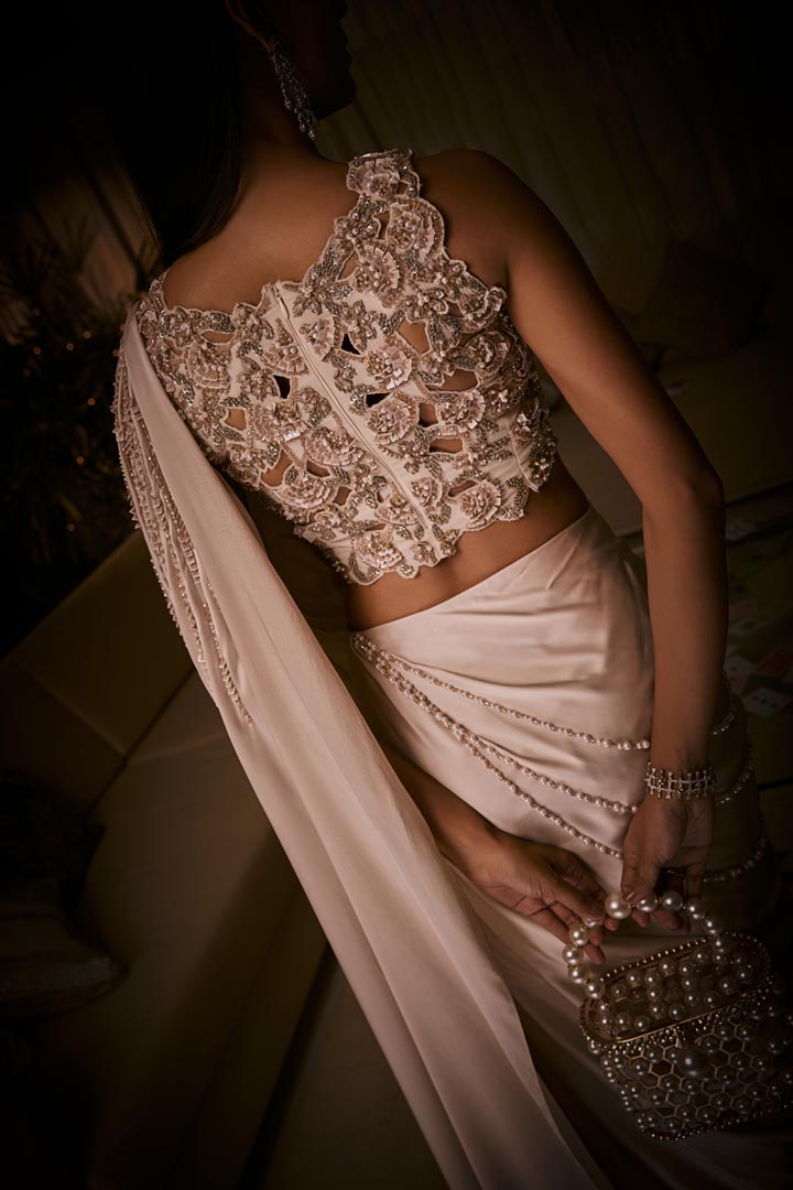 An ivory pre-draped saree in pure silk satin paired with a heavily hand-embroidered blouse featuring intricate pearl and sequin detailing.