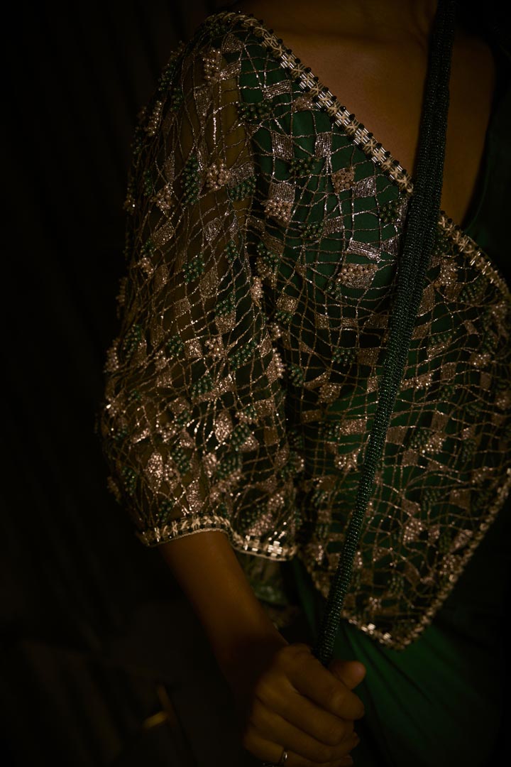An emerald green pure silk satin draped saree paired with an intricately embroidered tulle cape.