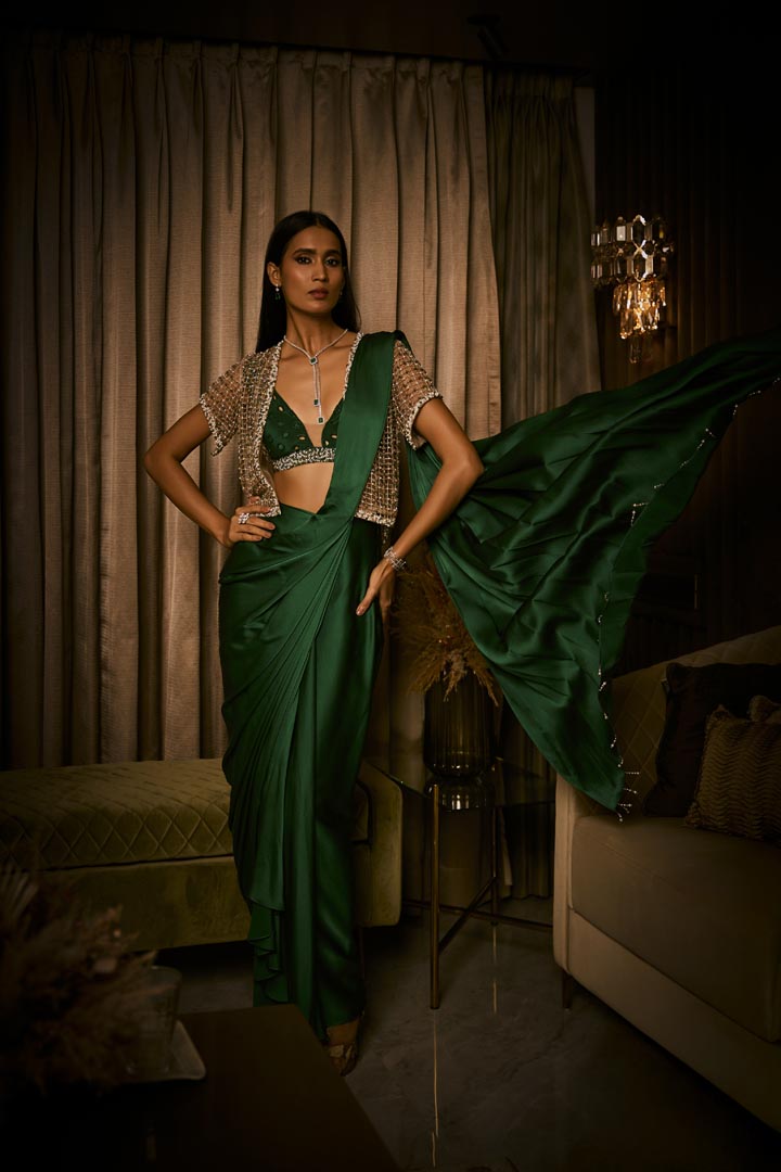 An emerald green pure silk satin pre-draped saree paired with a beaded bralette and embellished cutwork cape.