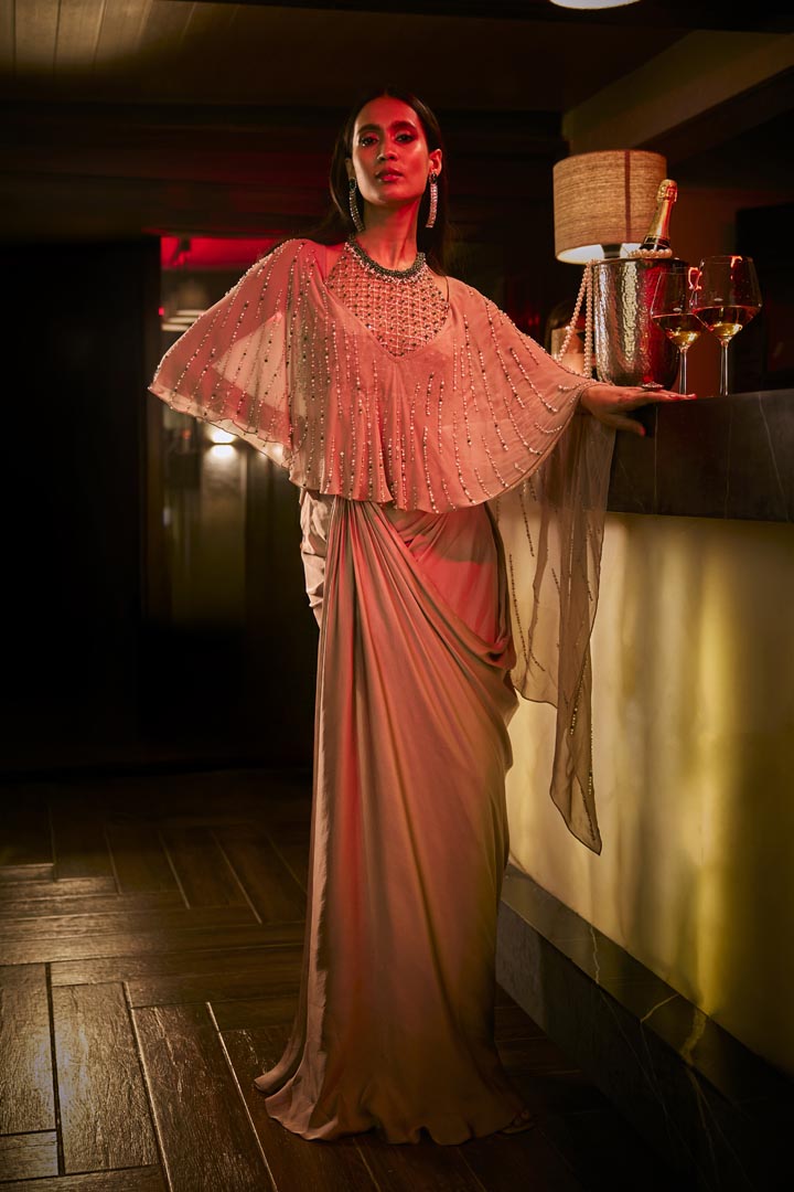 Taupe three-piece ensemble featuring a draped skirt, structured blouse, and a sheer embellished cape.