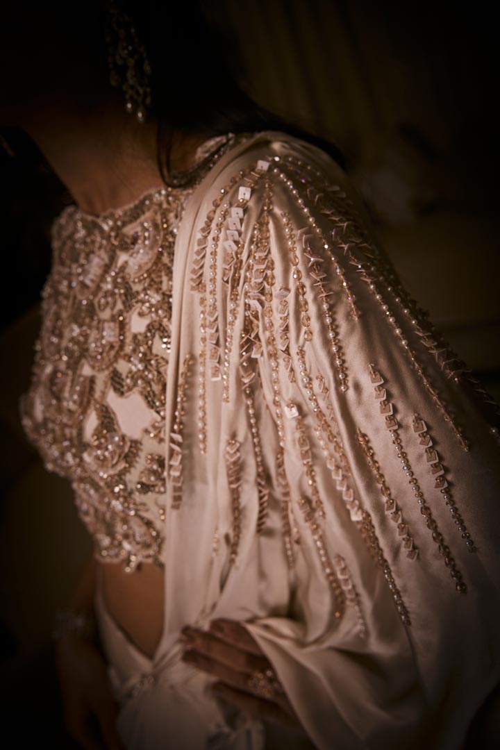 An ivory pre-draped saree in pure silk satin paired with a heavily hand-embroidered blouse featuring intricate pearl and sequin detailing.