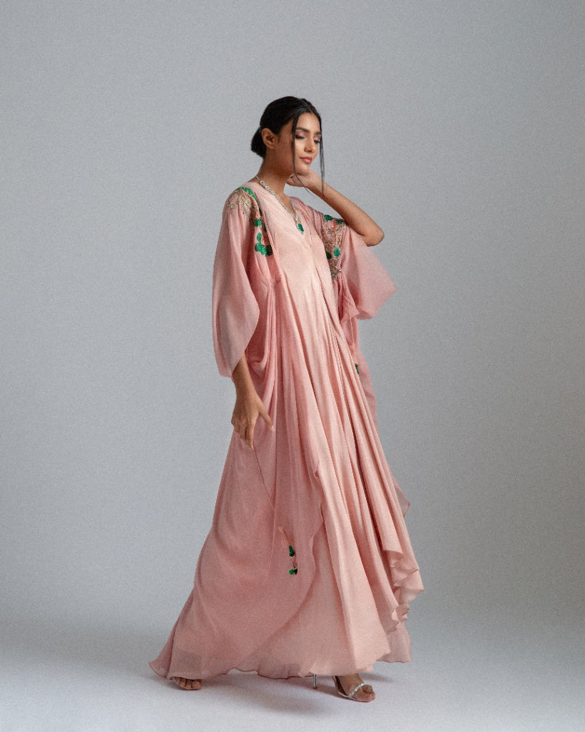 A Peach asymmetrical drape dress paired with a kaftan jacket featuring intricate green and champagne-toned floral embroidery and accentuated by a pleated box opening inner drape. 