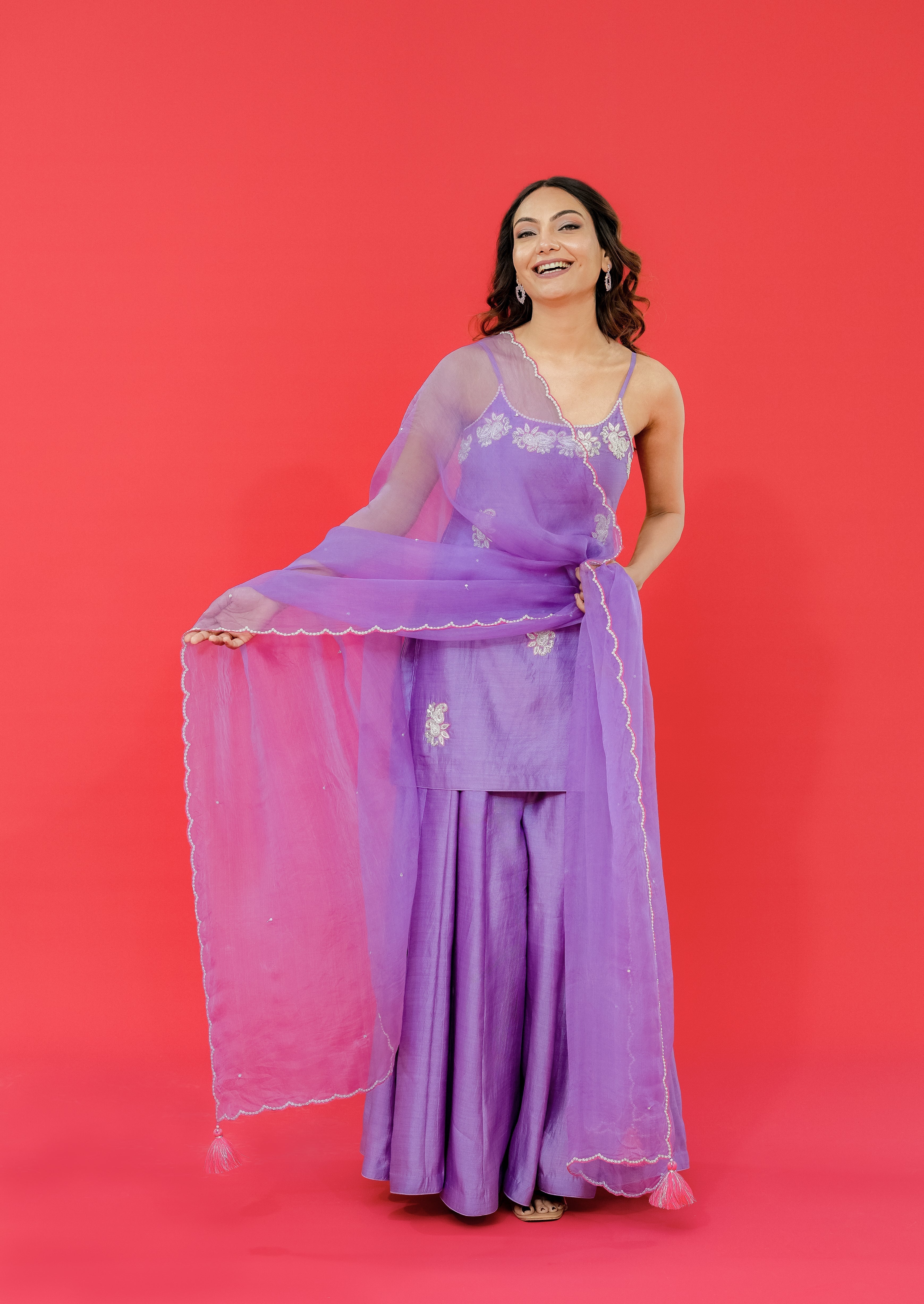 Woman in a purple traditional outfit with a sheer dupatta against a red background