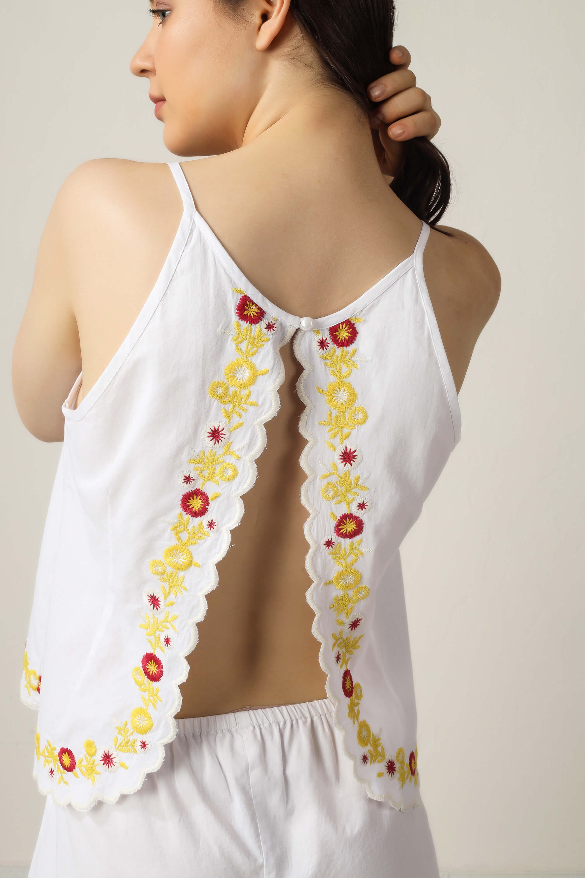 Elegant white camisole with floral embroidery and open back design.